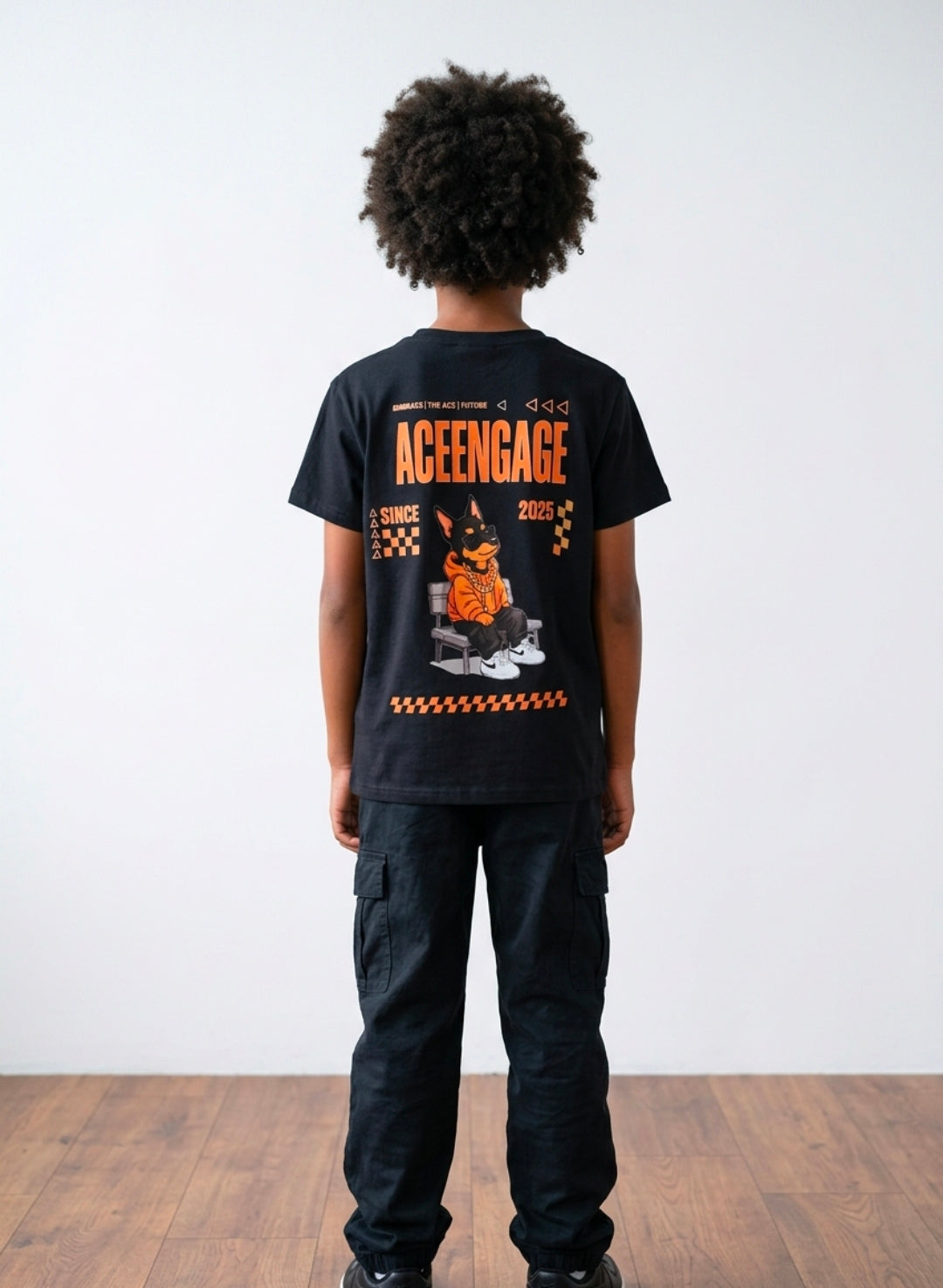 Back view of a child wearing a black AceEngage T-shirt with orange branding and a Doberman graphic